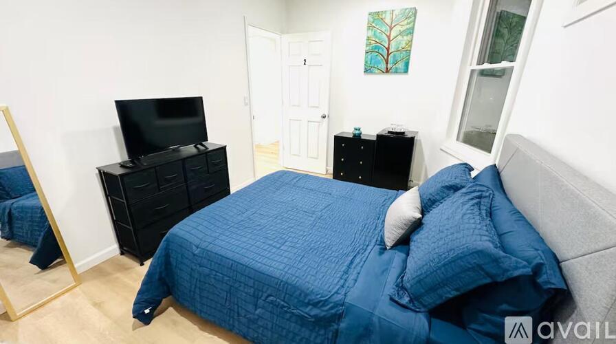 A bed with a blue comforter and pillows sits in a room with a television and a cabinet.