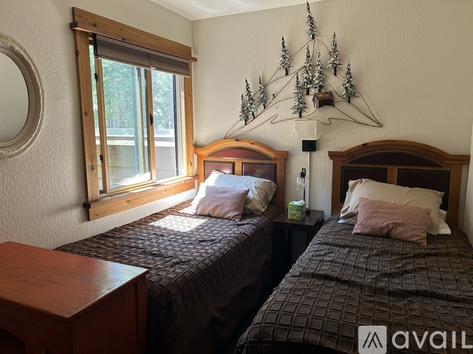 Two twin beds in a room with wooden headboards and a wall hanging of pine trees.