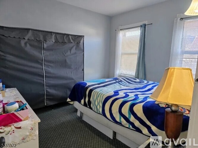 A bedroom with a bed, a nightstand with a lamp, and a window with curtains.