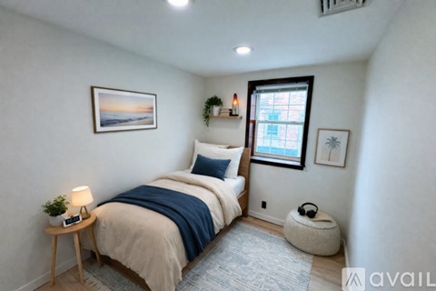 A bedroom with a bed, a nightstand, a window, and a plant.