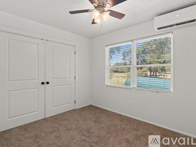 A room with a ceiling fan and a window showing a pool and trees outside.