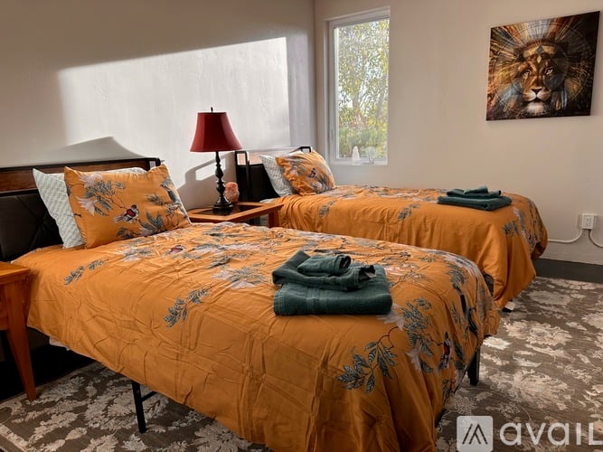 Two twin beds with orange bedspreads and matching pillows in a room with a lion painting on the wall.