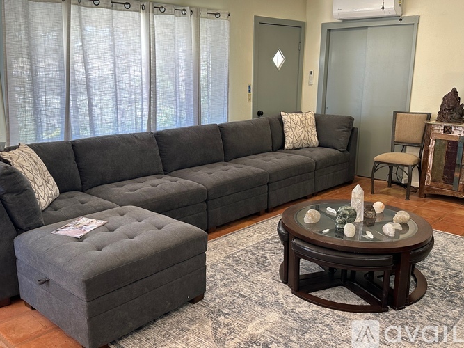 A grey couch with a grey ottoman in front of a glass table.