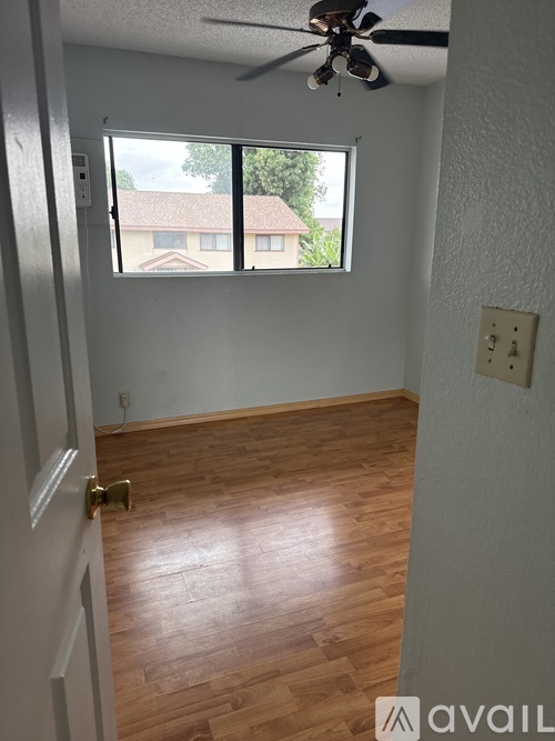 A room with a ceiling fan and a window overlooking a house.