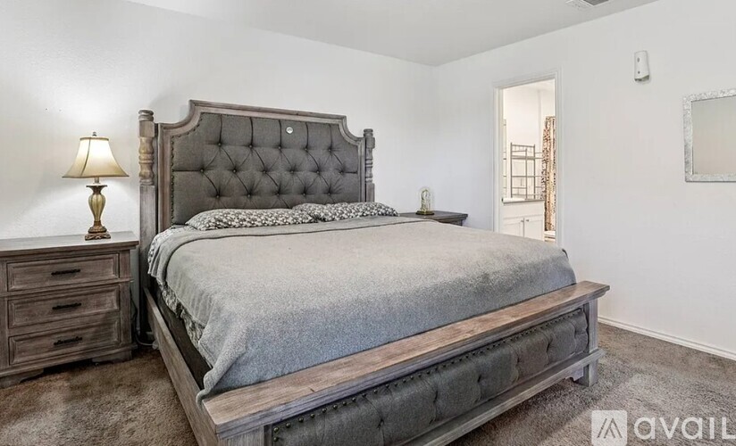 A bedroom with a large bed, wooden headboard, and a lamp on the nightstand.