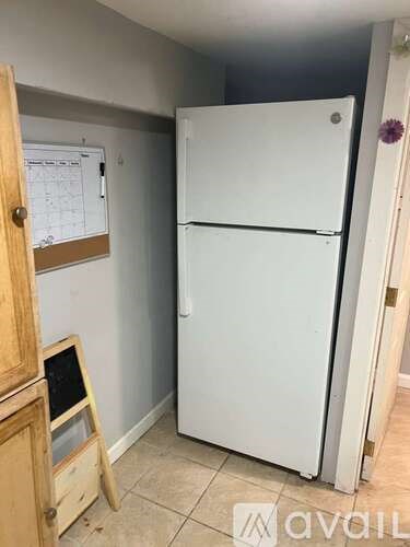 A white refrigerator in a kitchen with a wooden cabinet and a whiteboard on the wall.