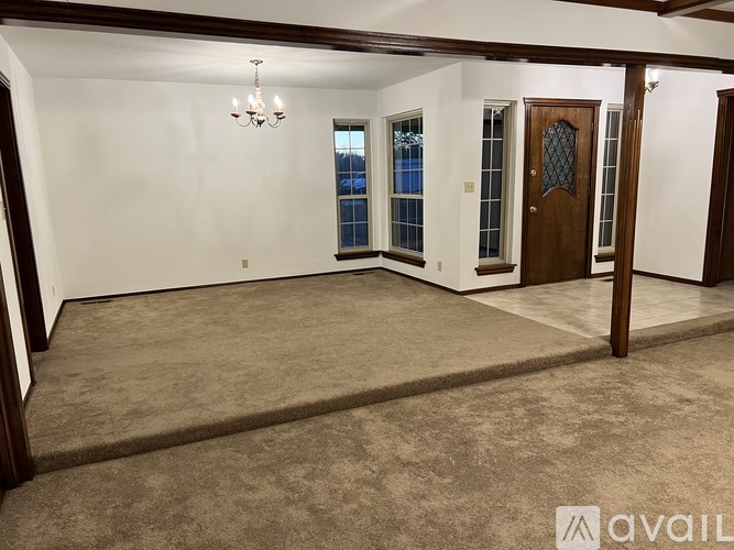 A room with a carpeted floor, a chandelier, and a door with a glass panel.