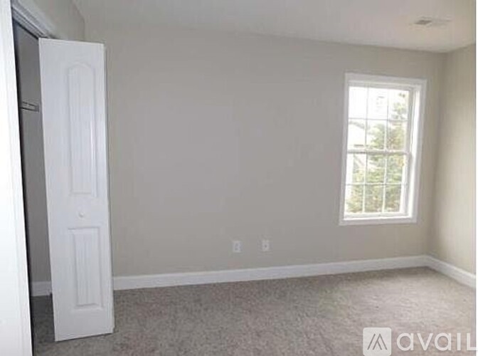 A room with a white door and a window with a view of trees outside.