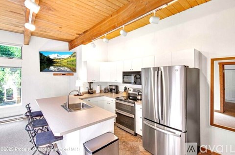A modern kitchen with stainless steel appliances and a wooden ceiling.