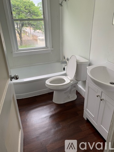 A white toilet in a bathroom with wooden floors and a window.