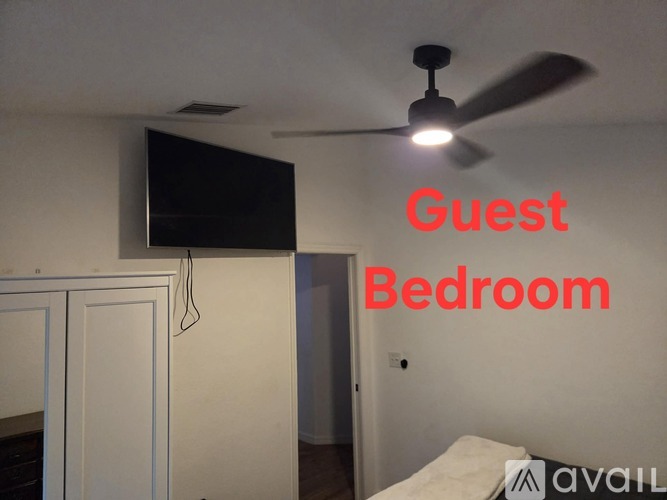 A guest bedroom with a fan and a television.