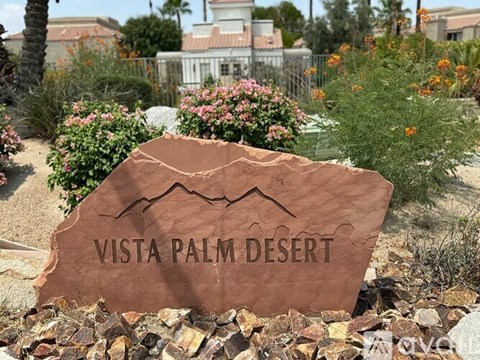A brown sign that says Vista Palm Desert in front of a garden.