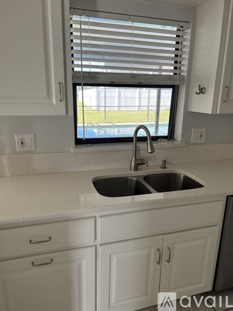 A kitchen with white cabinets and a window with blinds.