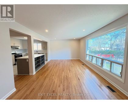 A spacious room with wooden flooring and a large window overlooking a street.