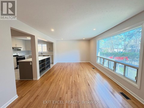 A spacious room with wooden flooring and a large window overlooking a street.