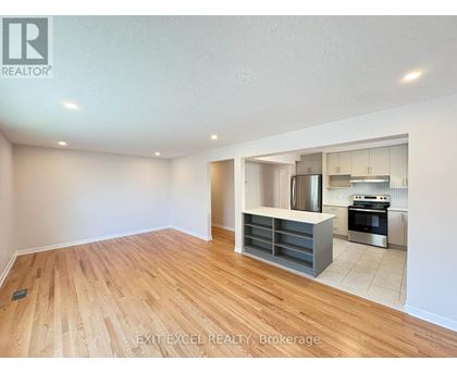 A spacious room with wooden flooring and a kitchen area in the background.