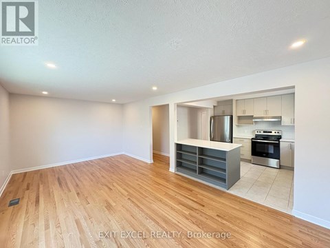 A spacious room with wooden flooring and a kitchen area in the background.