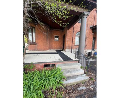 A red brick building with a black railing and a tree in front.