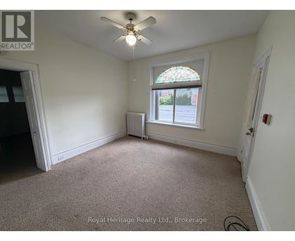 A room with a ceiling fan and a window with a view of the street outside.
