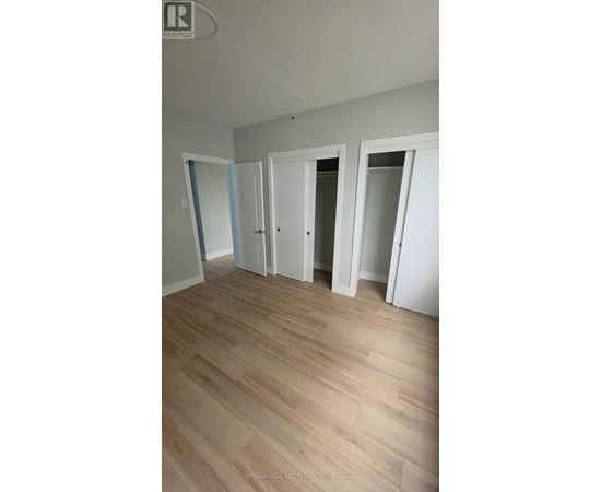 A room with white walls and wooden flooring with three doors.