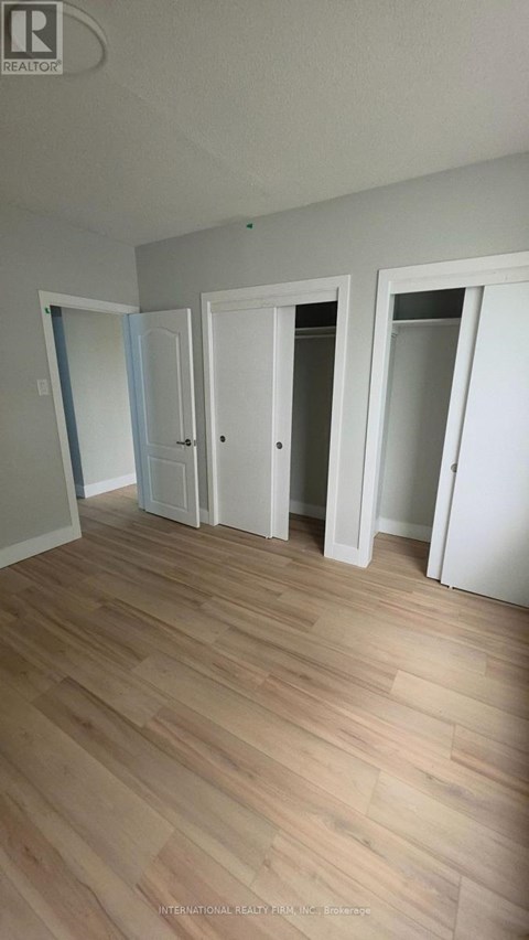 A room with white walls and wooden flooring with three doors.