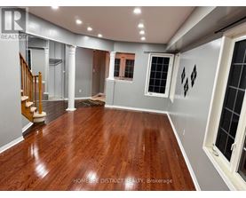 A spacious room with wooden flooring and a staircase on the left side.