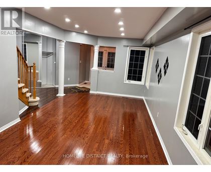 A spacious room with wooden flooring and a staircase on the left side.