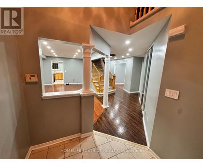 A hallway with a wooden floor and a staircase with a yellow railing.