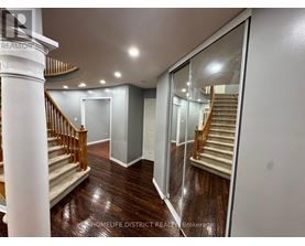 A spacious hallway with a wooden floor and a staircase with a wooden railing.