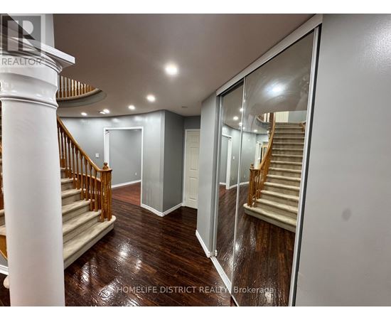 A spacious hallway with a wooden floor and a staircase with a wooden railing.