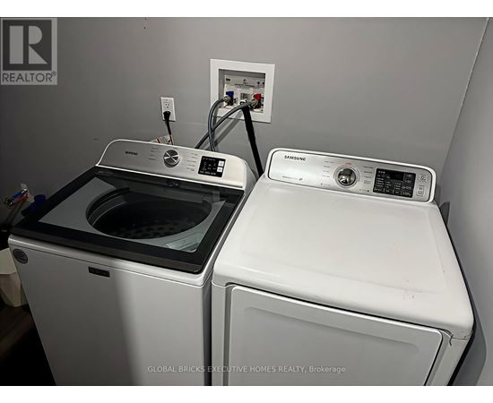 A Global Bricks Executive Homes Realty brochure is displayed on a wall above a washer and dryer.