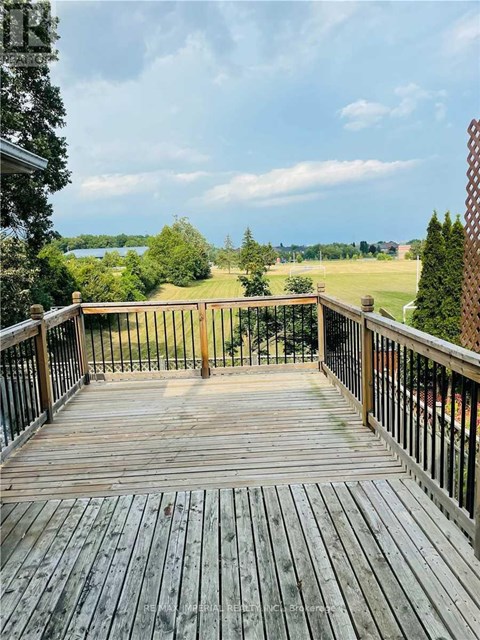 A wooden deck with a metal railing overlooks a grassy field.
