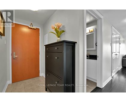 A brown door is on the left of a black cabinet with a vase of flowers on top.