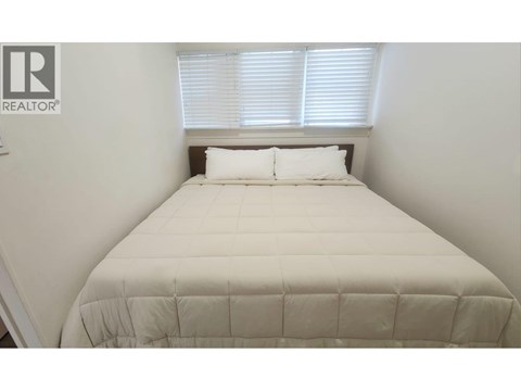 A bed with a white comforter and two pillows in a room with a window.