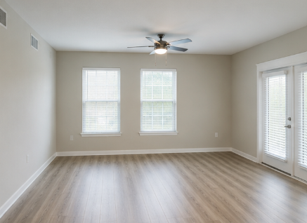 A room with a ceiling fan and two windows.