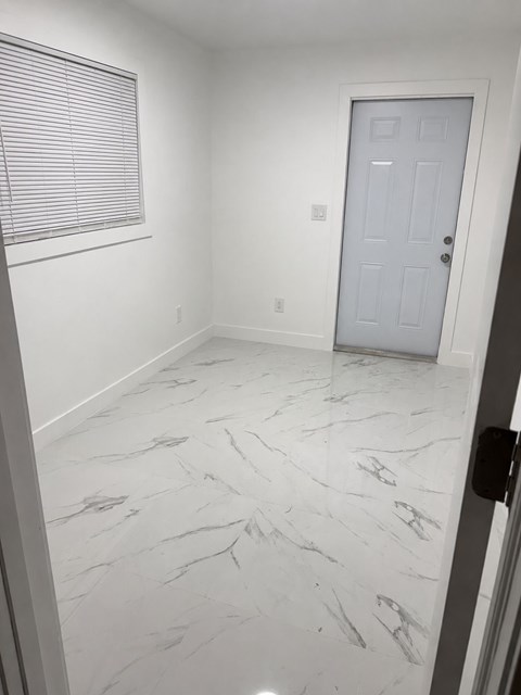 A white door is in a room with a marble floor.