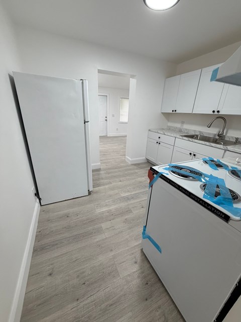 A kitchen with a white fridge and a white oven with blue tape on it.