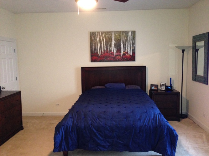 A bedroom with a bed, nightstand, and a painting on the wall.