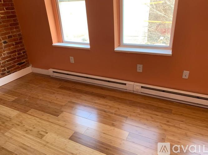 A room with wooden flooring and two windows.