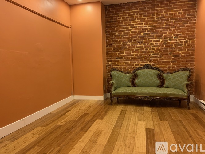 A green sofa sits against a brick wall in a room with wooden flooring.