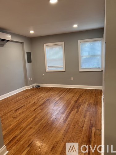 A room with wooden flooring and two windows.