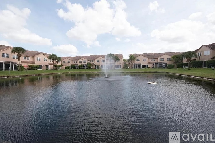 A fountain in the middle of a pond in front of apartment buildings.