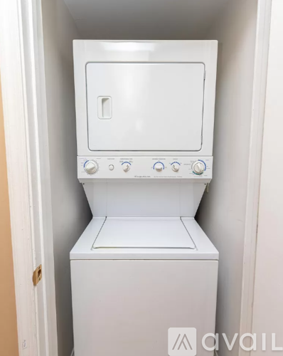 A white compact oven with a door and a control panel is installed in a small space.