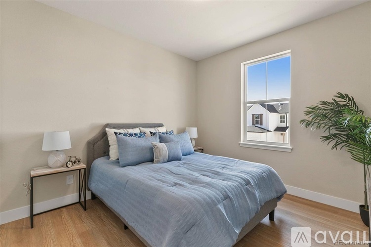 A bedroom with a bed, nightstand, and a window with a view of a house.