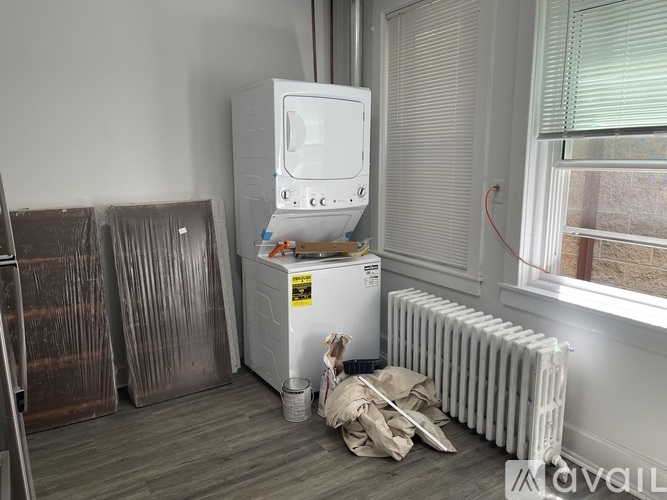 A white refrigerator is on top of a white radiator in a room with a window.