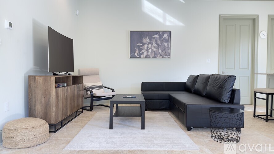 A modern living room with a black couch, a wooden entertainment center, and a glass coffee table.