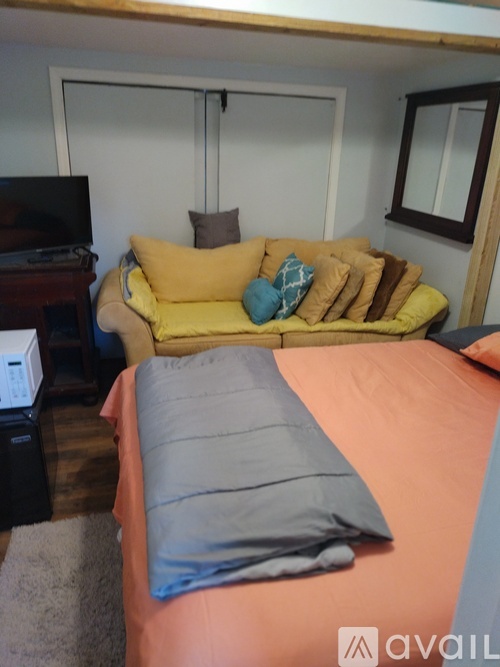 A bed with a grey pillow and a yellow couch with multiple pillows in a room.