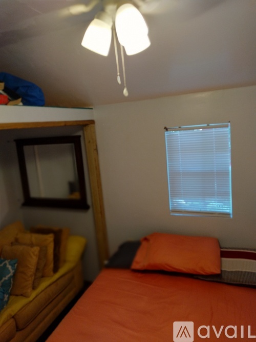 A bedroom with a bed, a couch, and a window with blinds.