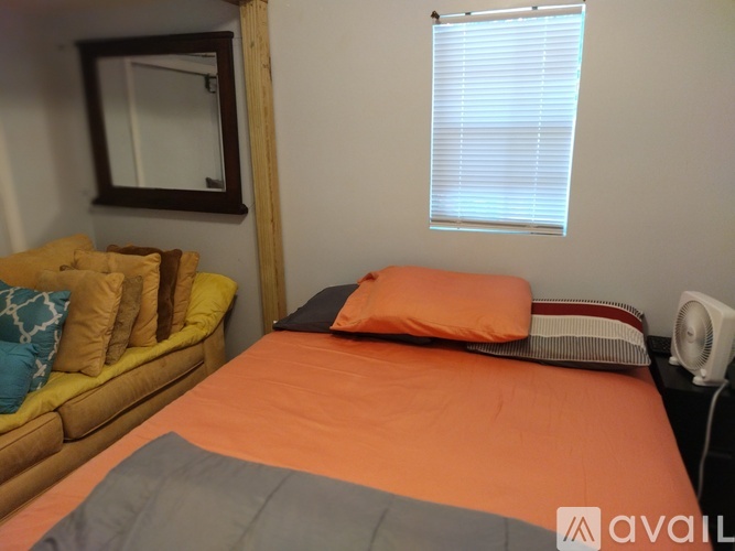 A bedroom with a bed, a couch, and a window with blinds.