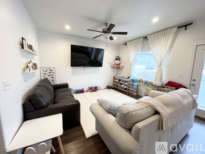 A living room with a couch, a chair, and a television mounted on the wall.